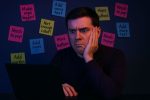 Дизайнер засмучено дивиться на ноутбук, оточений кольоровими стікерами з вимогами щодо редизайну сайту